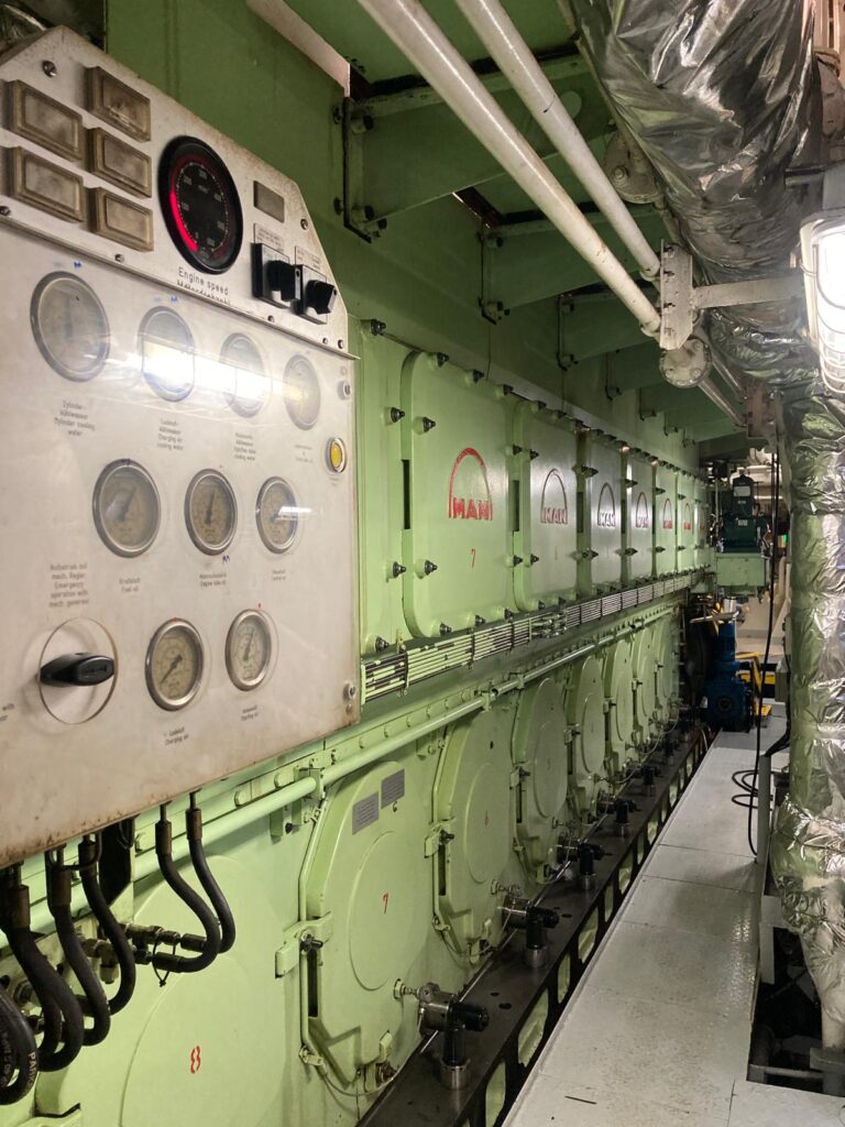 Großer MAN-Schiffsmotor mit Steuerpaneel im Maschinenraum.